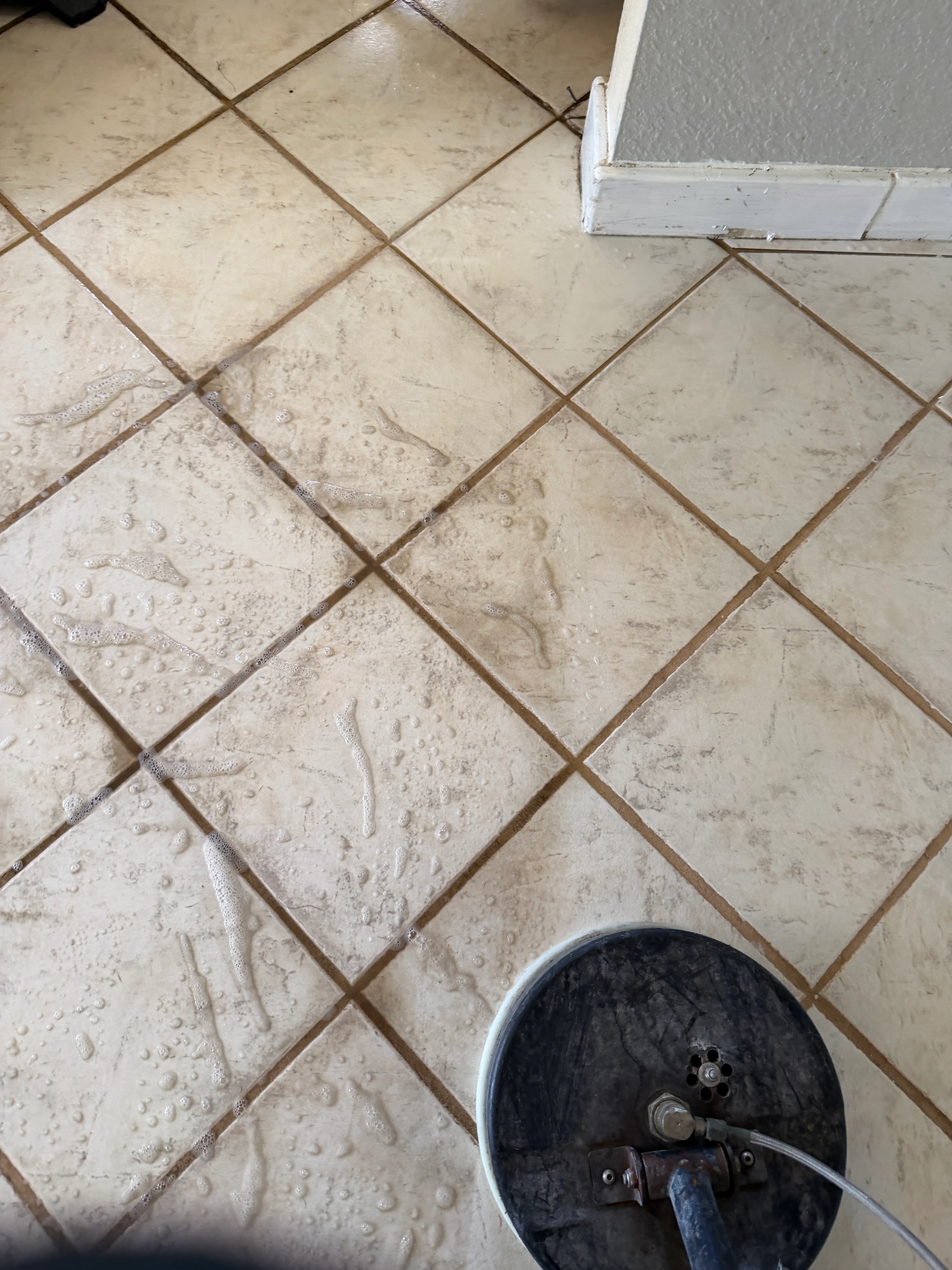 Ceramic tile floor with diagonal herringbone pattern and cleaned grout lines, polishing equipment visible
